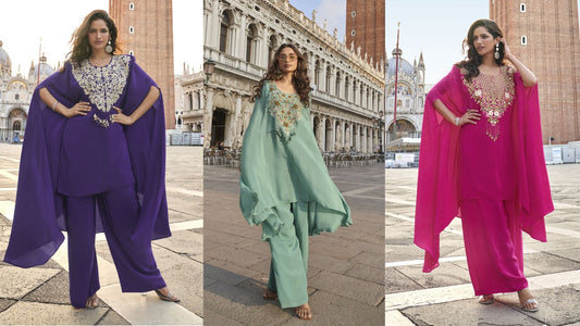 Three women in vibrant designer cape-style suits purple, aqua, and fuchsia posing elegantly in a historic European plaza for a luxury festive fashion showcase