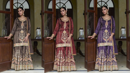 Three women wearing intricately embroidered ethnic sharara sets in brown, purple, and maroon, posing elegantly in a traditional doorway
