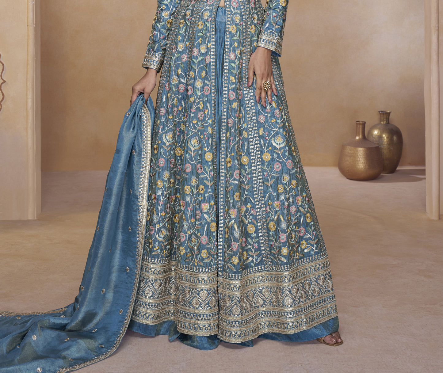 Woman in a blue patterned dress holding a matching dupatta in a neutral setting.

