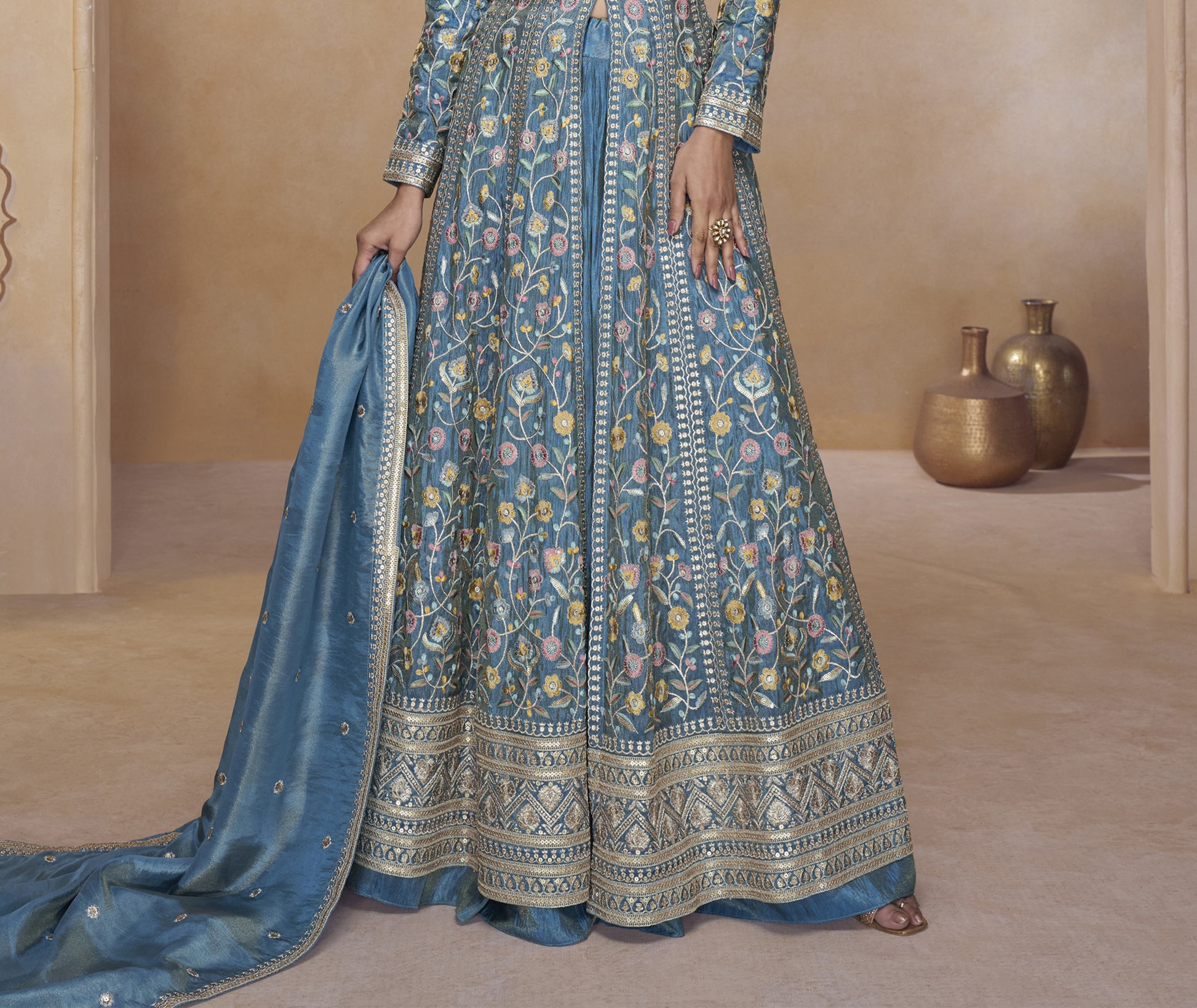 Woman in a blue patterned dress holding a matching dupatta in a neutral setting.

