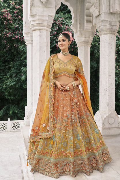 Close-up of a model in a mustard-orange embroidered bridal lehenga featuring intricate peacock work, zari details, floral dupatta, and traditional bridal jewelry