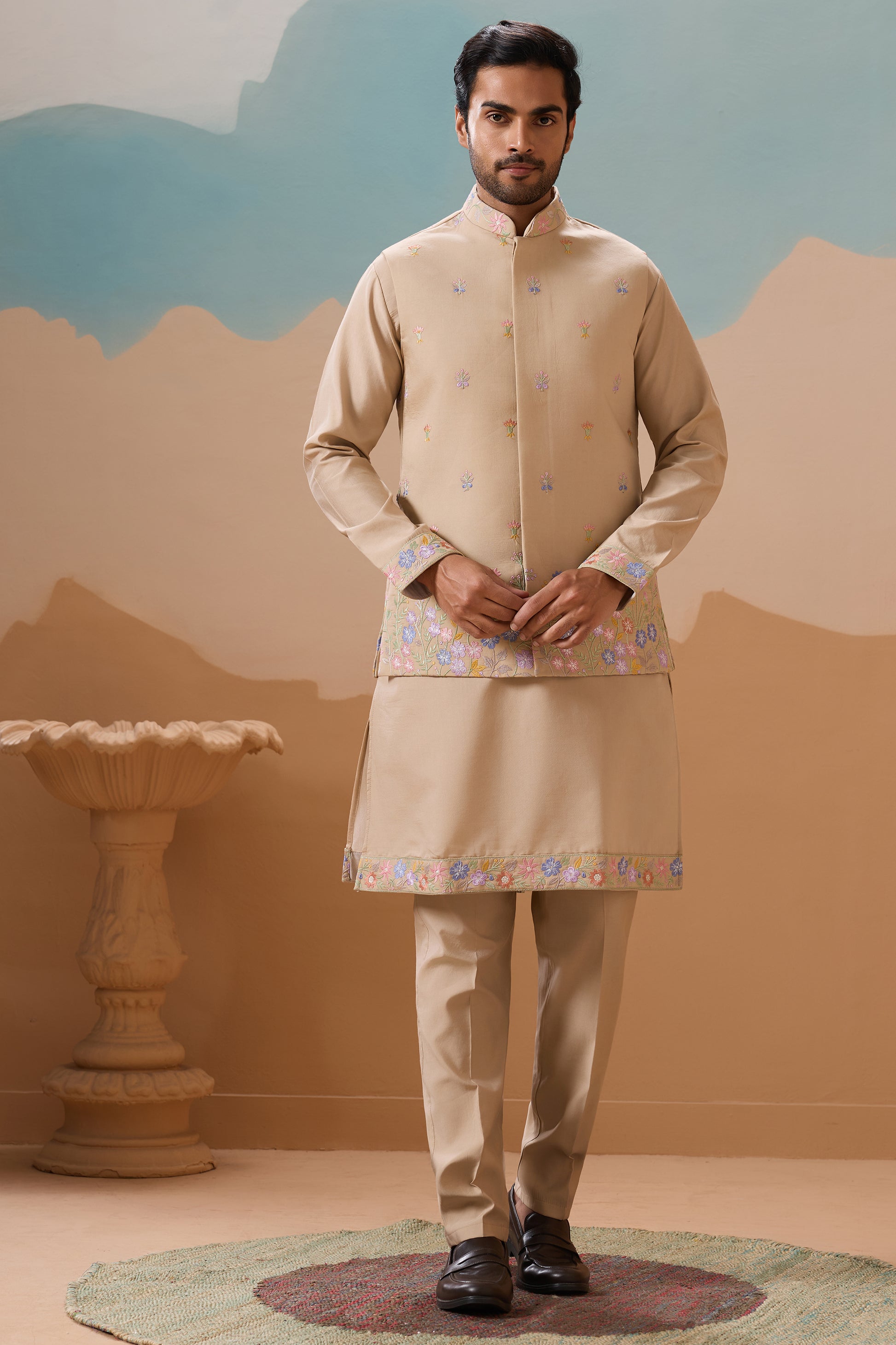 Man Wearing A Traditional Beige Outfit With Floral Patterns Against A Desert-Themed Backdrop

