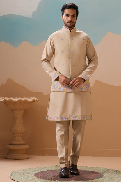 Man Wearing A Traditional Beige Outfit With Floral Patterns Against A Desert-Themed Backdrop

