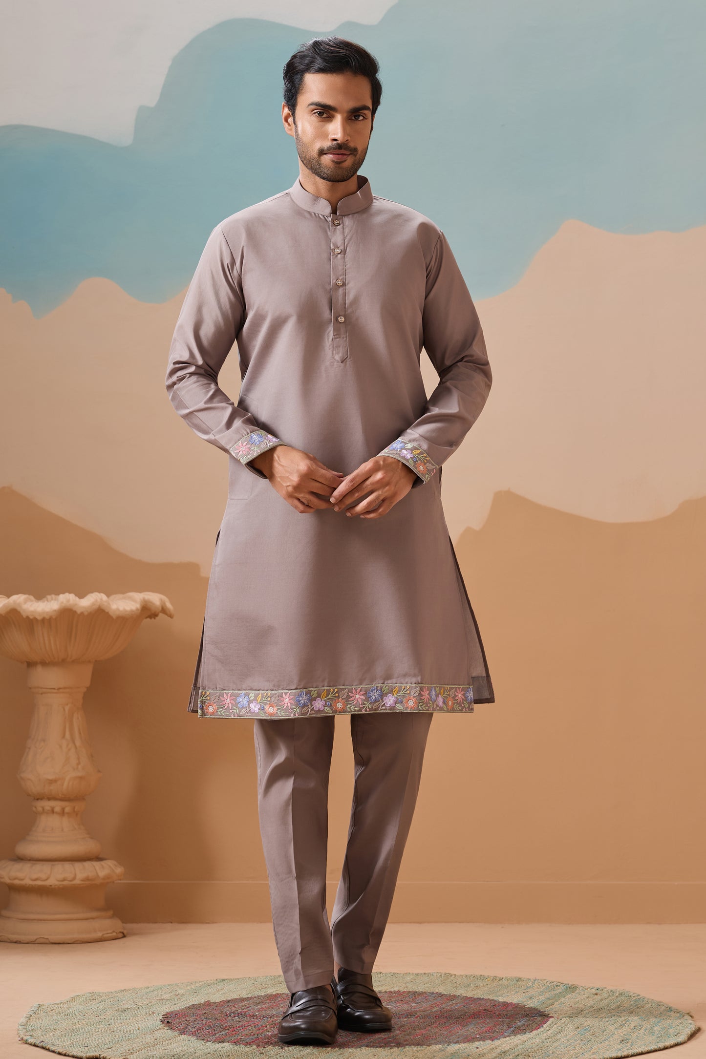 Man Wearing A Traditional Kurta With A Decorative Hemline Against A Sylized Landscape Background
