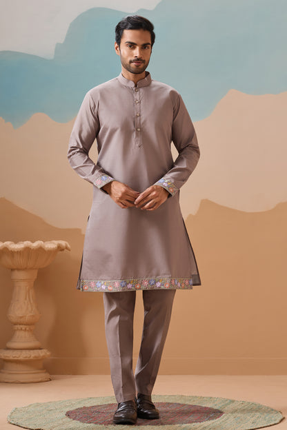 Man Wearing A Traditional Kurta With A Decorative Hemline Against A Sylized Landscape Background
