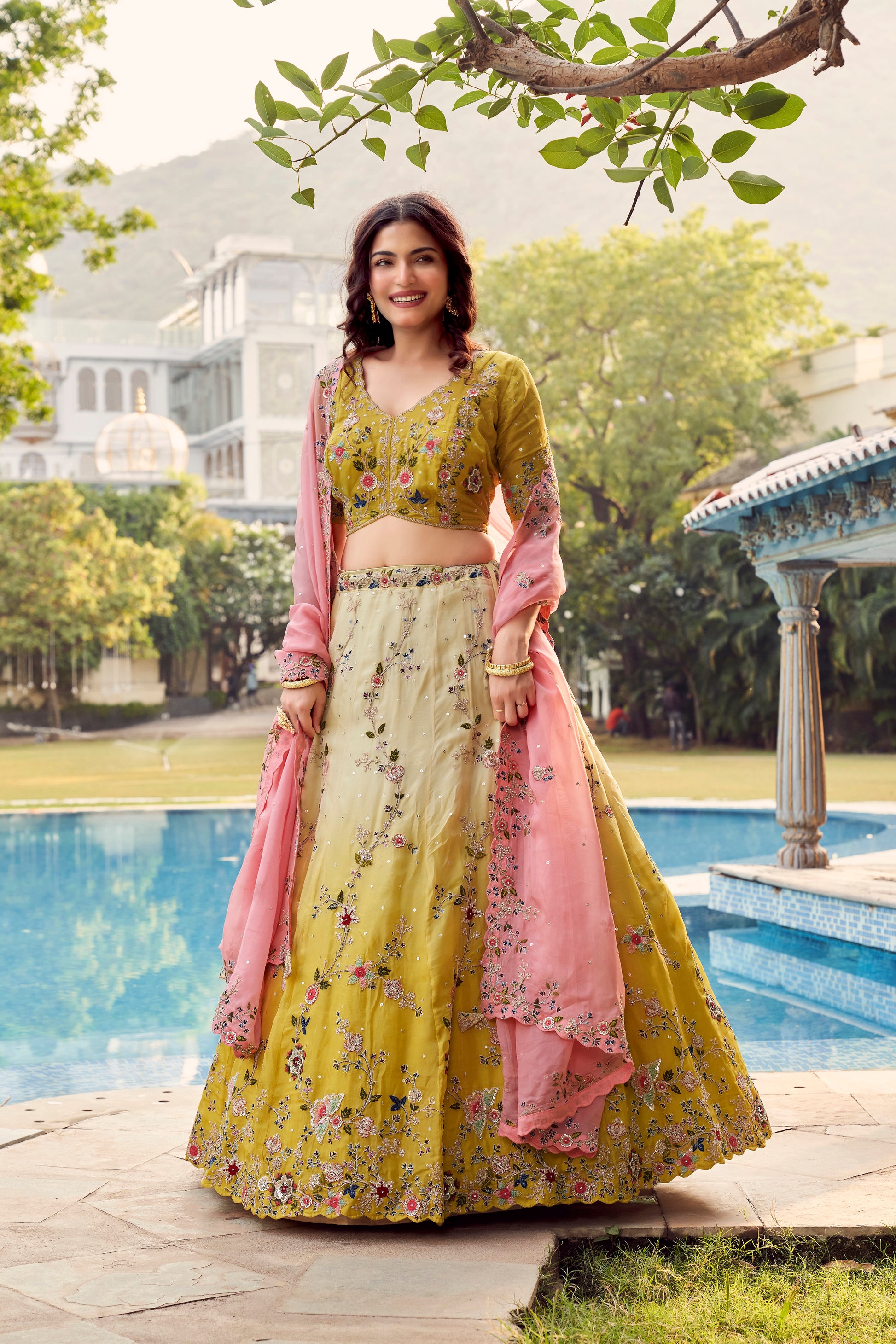 Elegant Yellow Lehenga With intricate Floral Work and Pink Dupatta Worn By a Smiling Woman.