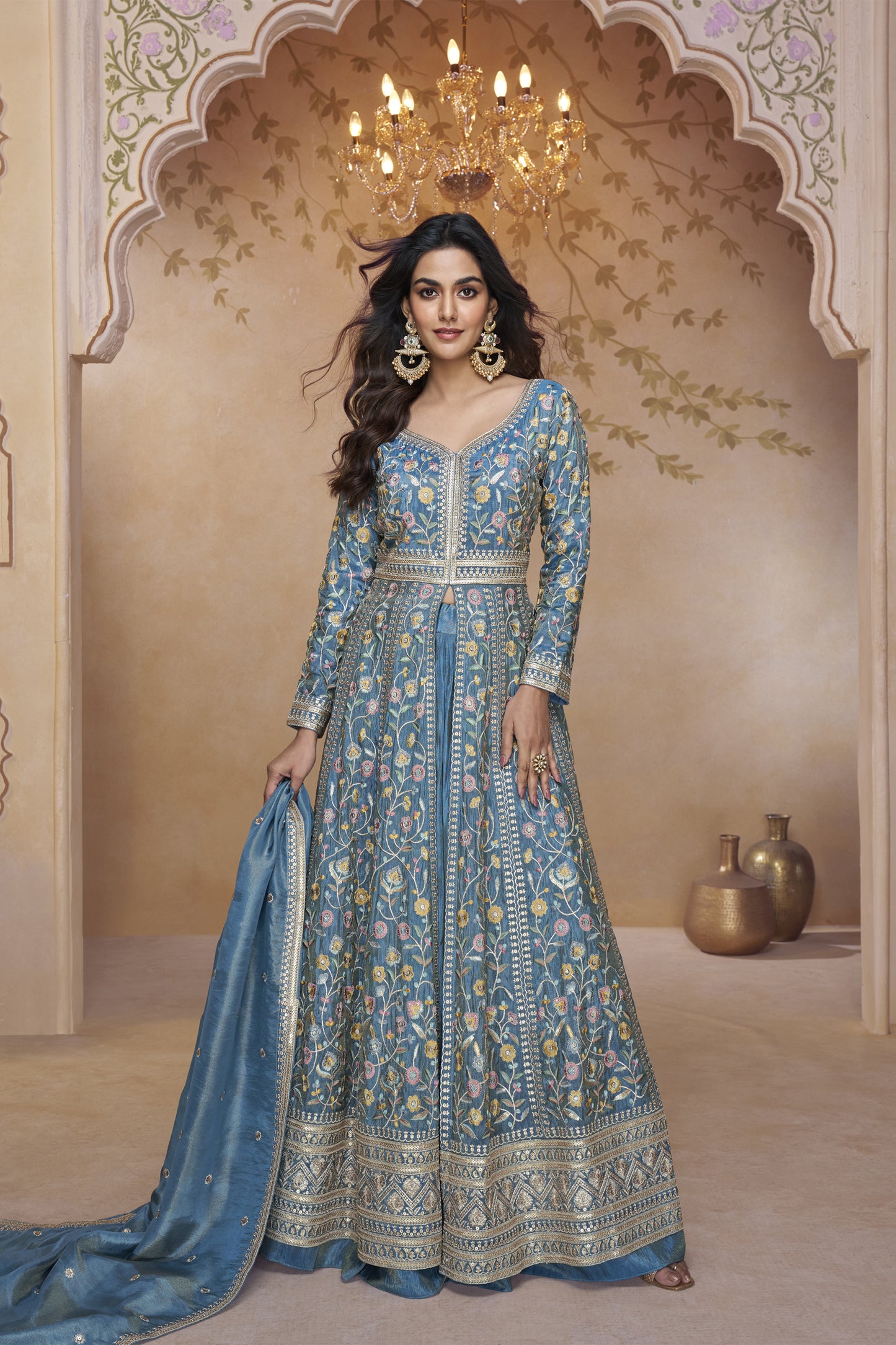 Blue embroidered floor-length gown with detailed floral work, long sleeves, and matching dupatta worn by a woman at a royal backdrop.