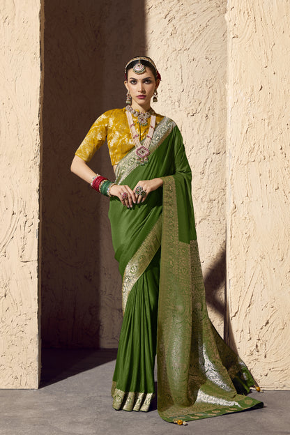 Woman wearing a green silk saree with gold zari border and mustard yellow brocade blouse, styled with traditional Indian jewelry, bangles, and hair accessories.
