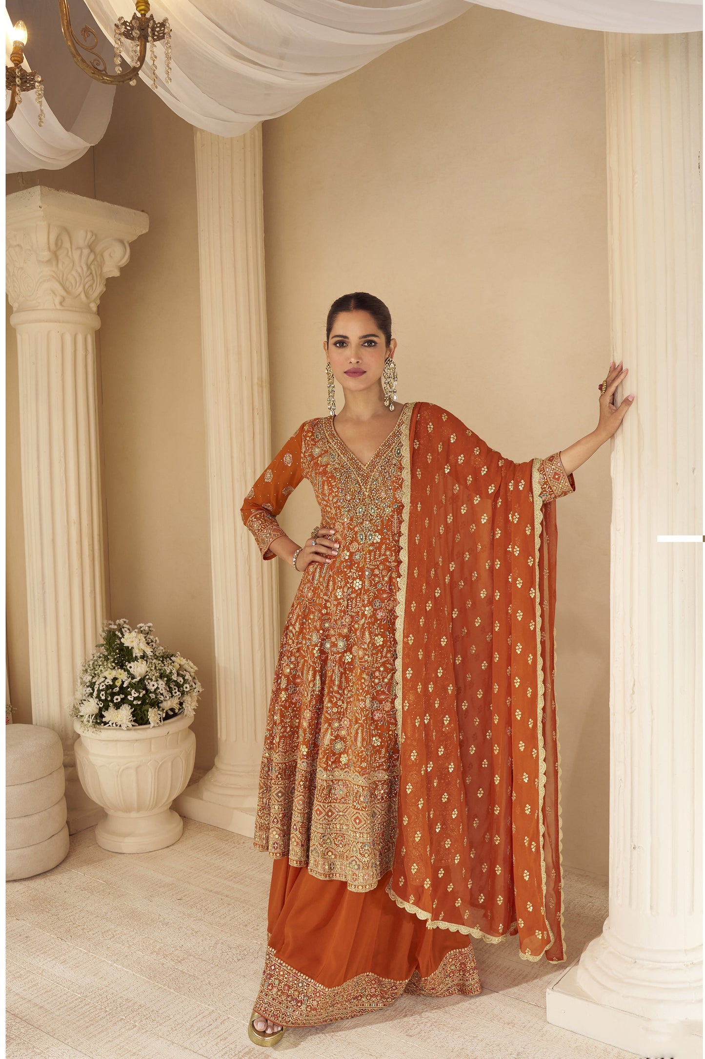 Woman wearing rust orange embroidered sharara suit with heavy zari and mirror work