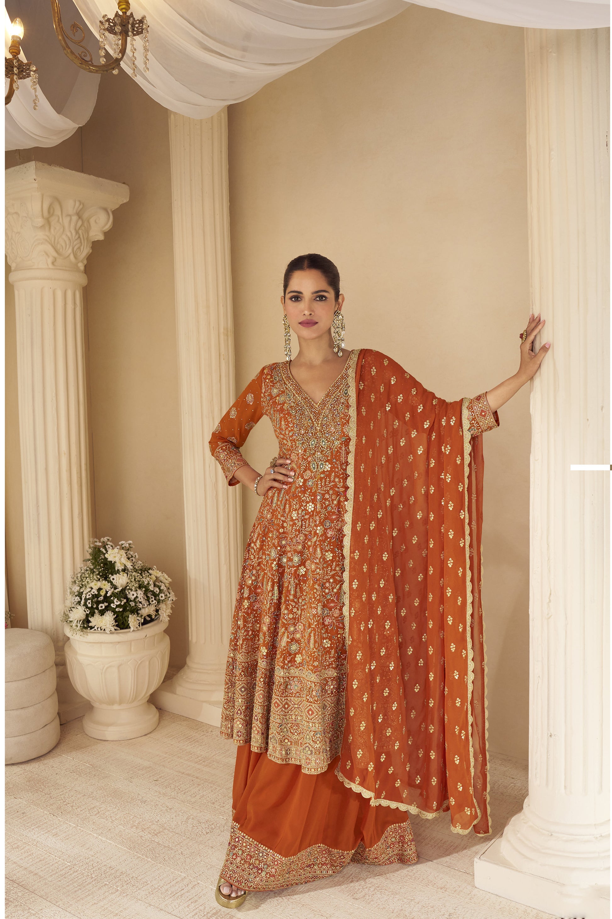 Woman wearing rust orange embroidered sharara suit with heavy zari and mirror work