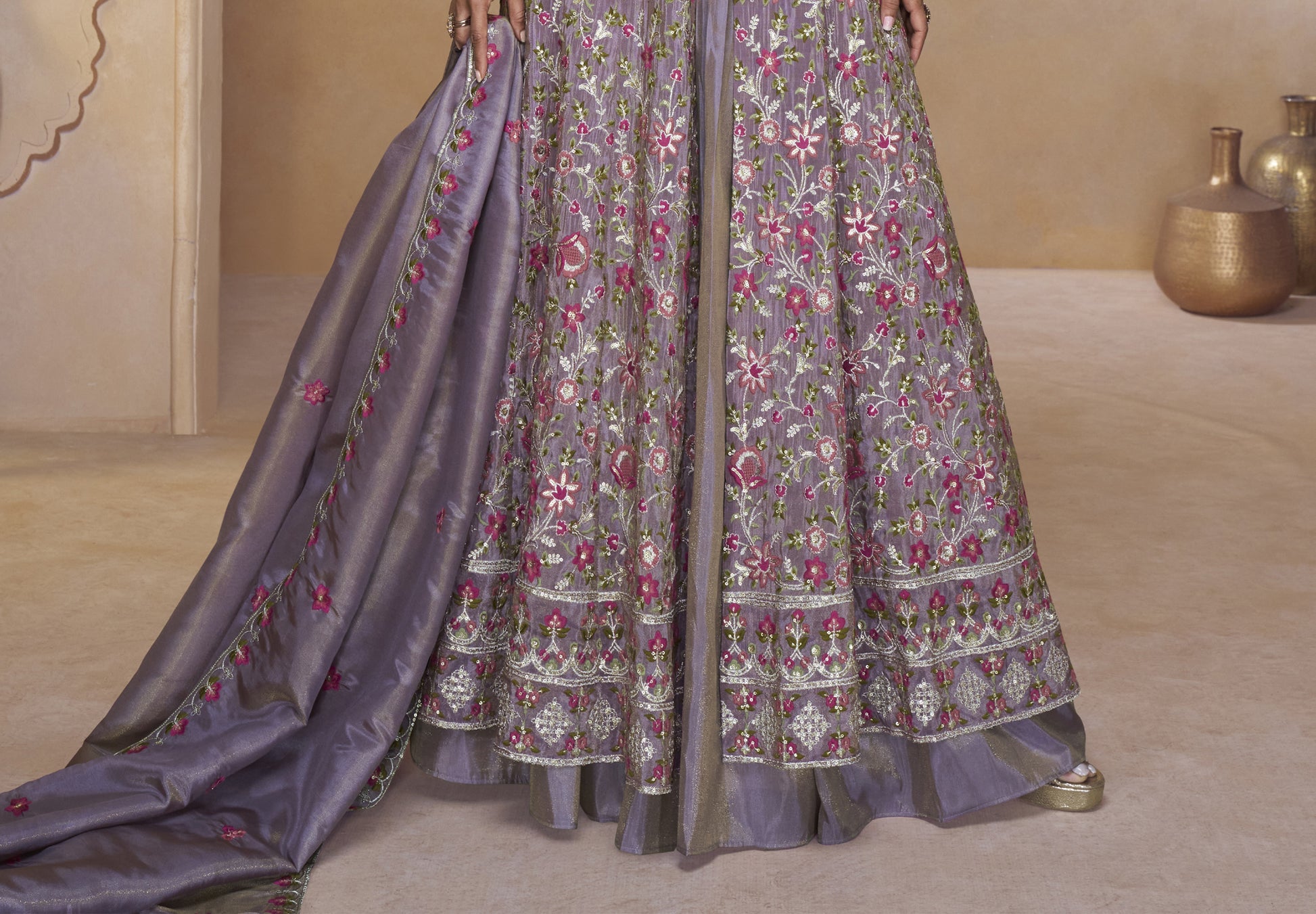 Elegant mauve-purple full-length gown with heavy ethnic embroidery paired with statement earrings in a palace-themed setting