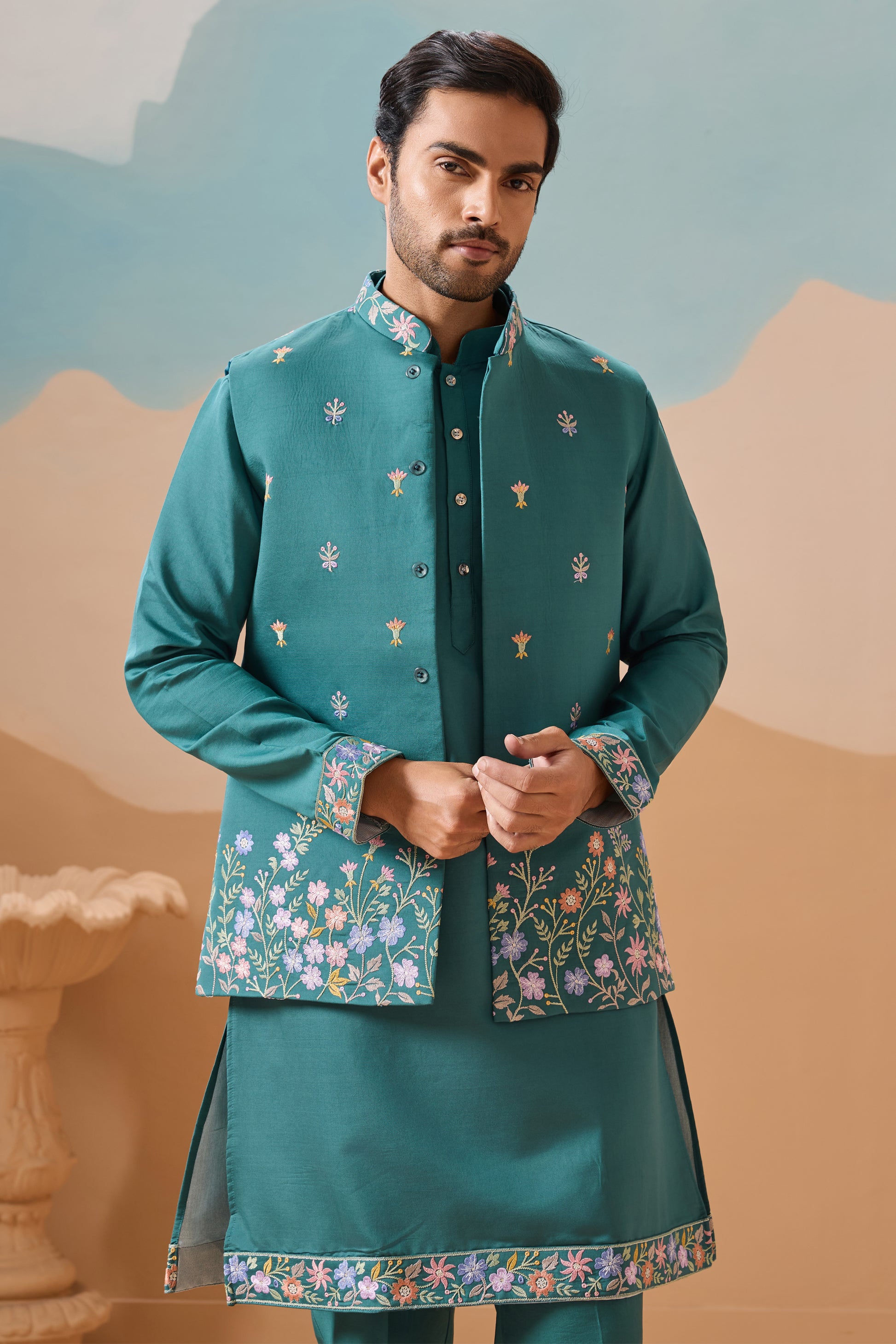 Man wearing a traditional green embroidered outfit with a scenic background