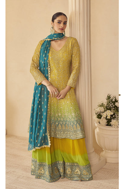 Woman wearing a yellow and blue traditional outfit with a matching dupatta against a beige wall.
