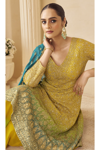 Woman in a yellow and green embroidered traditional outfit with a blue dupatta.
